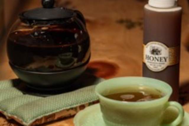 A cup of tea, teapot, and a bottle of "The Honey" on a wooden table with decorative etchings.