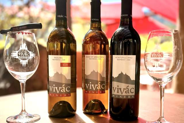 Three bottles of Vivác Winery wine lined up in a row, next to two wine glasses.