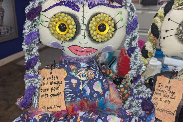 A colorful doll dressed in a vibrant patterned dress with a quote: "A witchy woman will always turn pain into power."