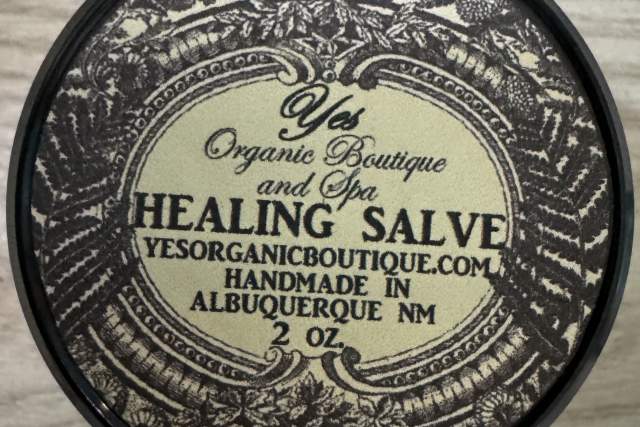 Top view of a round, ornate container from "Yes Organic Boutique Healing Salve" with intricate patterns, featuring text and the year 2012, Albuquerque, NM.