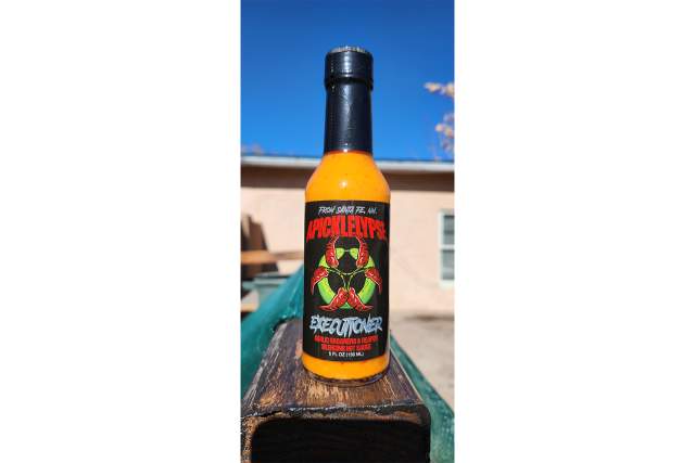 bright orange hotsauce in a clear bottle with a black label highlighted by red chiles in the shape of a hazardous symbolreading: From Santa Fe, Apickalypse Executioner, Garlic Habenero & Reaper Silencing Hot Sauce