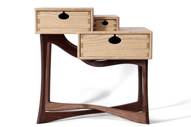 an abstract white wooden side table with three drawers sits in front of a white background