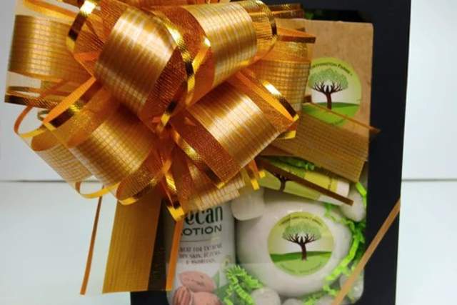 A gift box adorned with a large ribbon. Inside, visible items include a small bottle and a bar of soap with a tree logo on the packaging.
