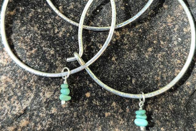 Three silver hoop earrings with turquoise beads lying on a speckled surface.