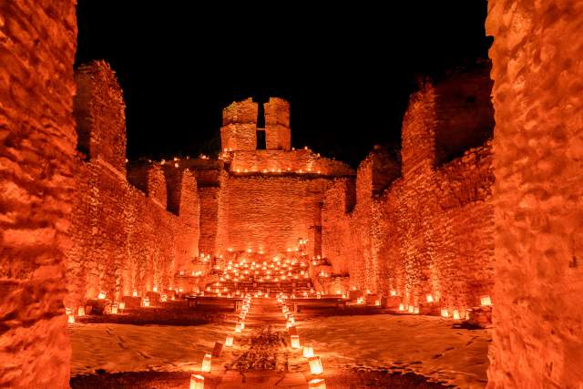 A set of stone ruins illuminated by many farolitos or luminarias.