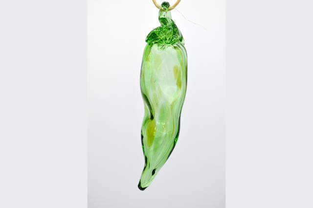 A delicate, green glass chili pepper ornament hanging against a plain white background.