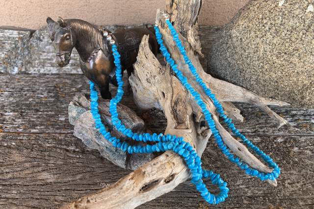 two beaded turquoise necklaces rest on a wooden stump