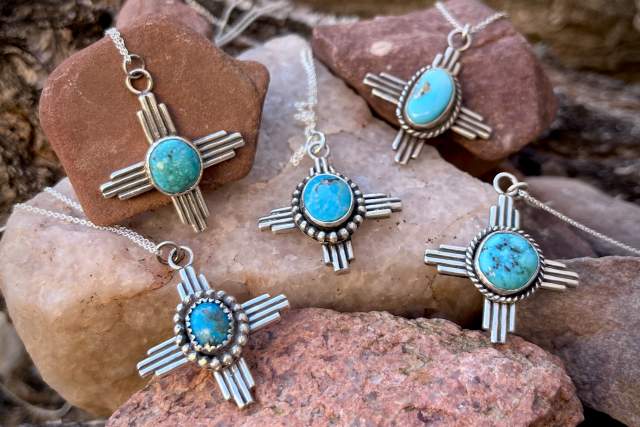 five silver zia shaped earrings with a turquoise center stone rest on an assortment of rocks