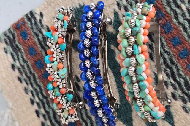 Three decorative hair clips with colorful beads and floral designs displayed on a patterned fabric.