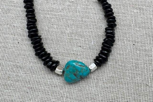A necklace with black beads and a large turquoise pendant, displayed on a textured background