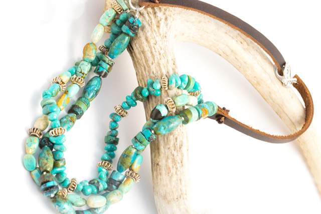 a beaded turquoise necklace with a leather strap sits on a white, bone like structure