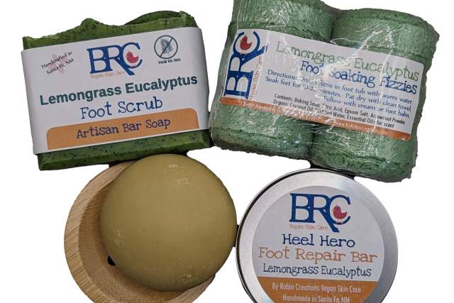 Four different hand-made body care products in green, tan and white packaging. All reading Lemongrass Eucalyptus, one is a foot scrub, one a foot soak, one a foot repair bar.