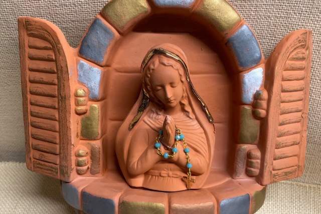 a red clay sculpture of a woman praying inside an opened window arch sits on a linen background