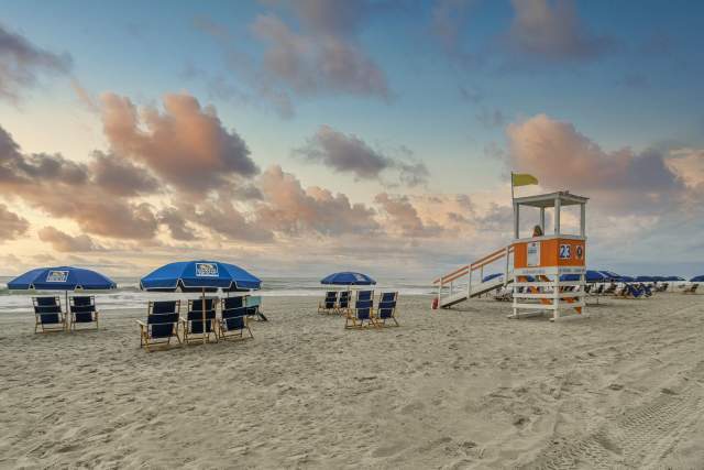 A beautiful sunrise in North Myrtle Beach with beach chairs, umbrellas, and lifeguard stand.