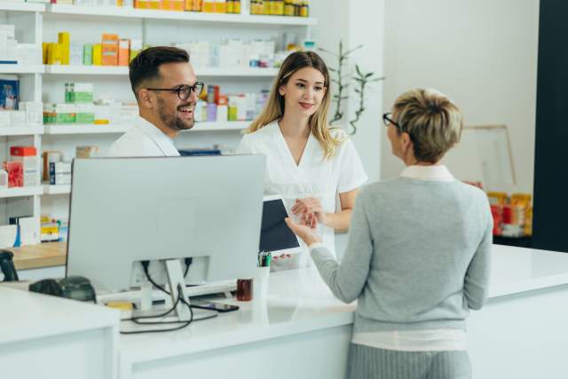 Two employees helping a customer at a pharmacy.