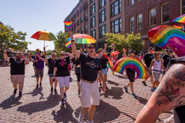 People marching and holding rainbow colored umbrellas at Heartland Pride Parade.