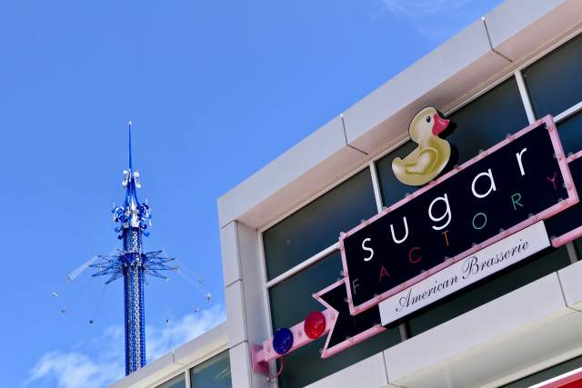 Close up of Sugar Factory signage, an ICON Park restaurant, with the StarFlyer in flight in the background.