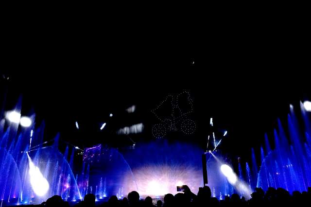 Drones form a character silhouette above a lagoon during a nighttime show at Universal Studios Florida, accompanied by illuminated fountains and lighting effects. Guests gather along the waterfront as water features, pyrotechnics, and synchronized lighting create a coordinated performance environment.