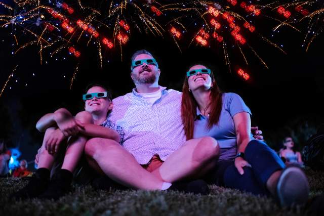 A family wearing 3-D glasses smiles up at fireworks, which appear to transform into LEGO bricks as they explode