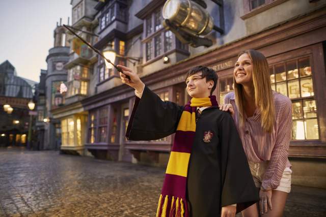 boy dressed as Harry potter waves wand while mom watches