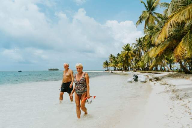 Pareja de adultos mayores con equipo de snorkel caminando por la playa de la Isla San Blas Guna Yala, Panamá