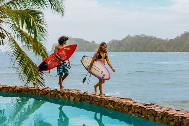 Couple walking near a pool with surfboards, Isla Grande beach can be seen in the background