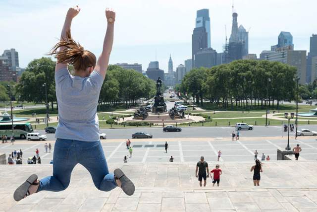 A women jumping in front of the Philadelphia skyline