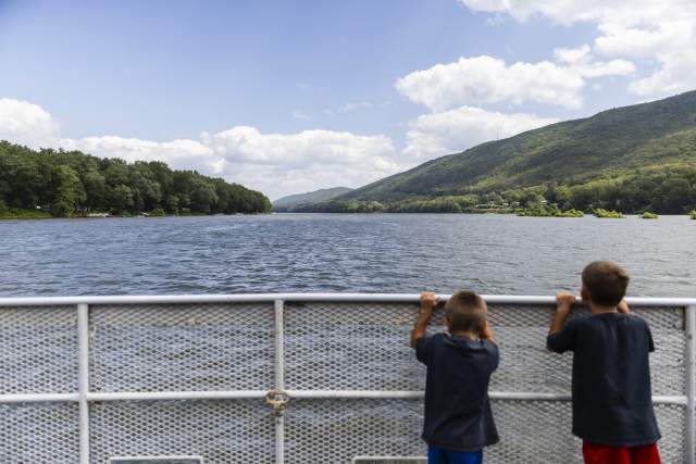 Two young boys looking over a railing on a boat that floating on a lake