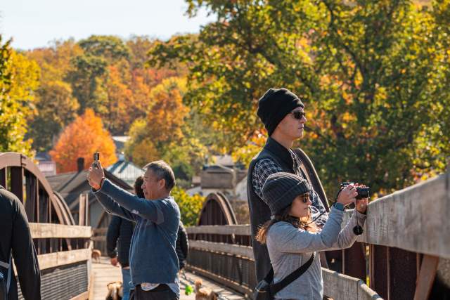 People standing on a bridge taking pictures with cameras of the surrounding fall foliage