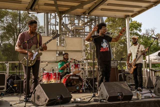 Four black men in a band on a stage performing for a crowd