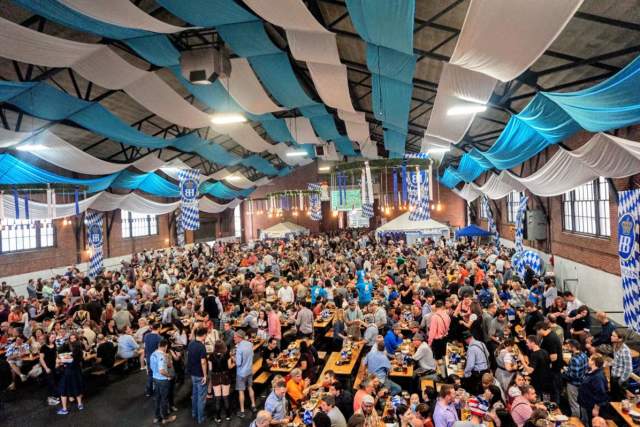 Aerial view of a beer festival being held inside with a lot of people under a blue and white striped roof