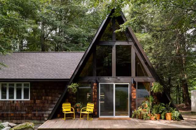An A-Frame cottage with two yellow chairs on a patio in front