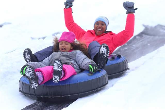 Little girl and woman in winter gear snowtubing down a snow covered hill at Camelback Mountain Resort in Tannersville
