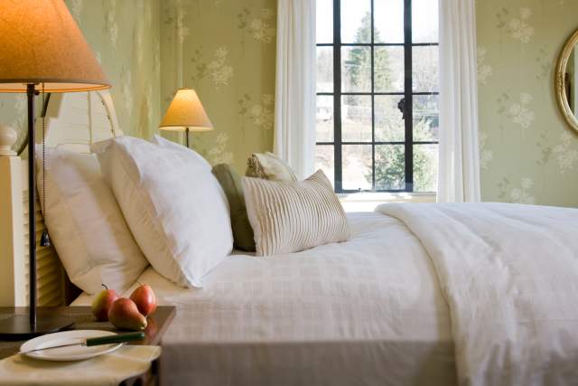 A made queen bed with apples and a plate and knife on the side table