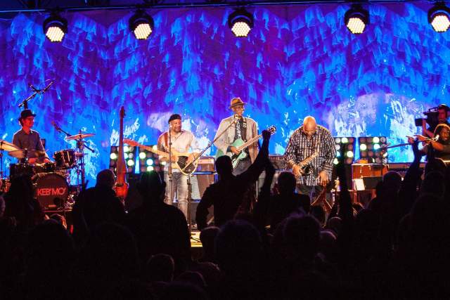 A band on a stage with silhouettes of people cheering in front of them