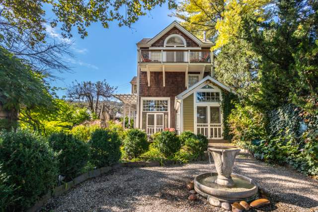 An exterior of a quaint bed and breakfast mansion with a fountain in the front and trees framing the front entrance