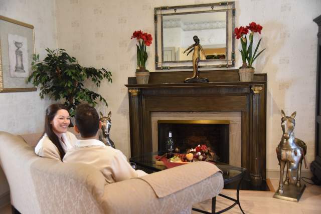 Man and woman sitting on a couch in front of a lit fireplace and a table with two glasses of wine