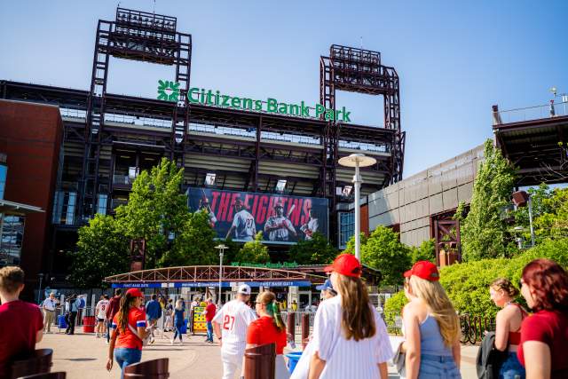 People wearing red hats and summer attire walking into the front entrance of Citizens Bank Park in Philadelphia