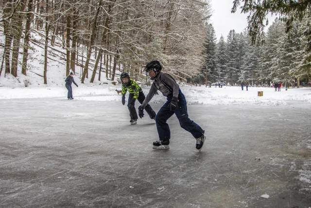 Two young boys with helmets on skating on a frozen pond in Cook Forest State Park