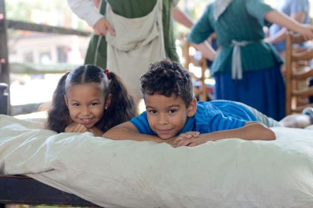 Two kids lying on a mattress and smiling at the camera