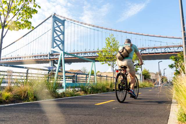 A person riding a bike on a trail with a large bridge in the background