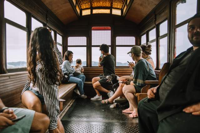 A group of 8 people in a small train car with everyone turning their backs to see the view out the window