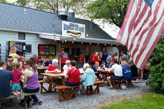 Groups of people sitting at picnic tables outside a restaurant storefront with the signage Eddie's Footlong Hot Dogs