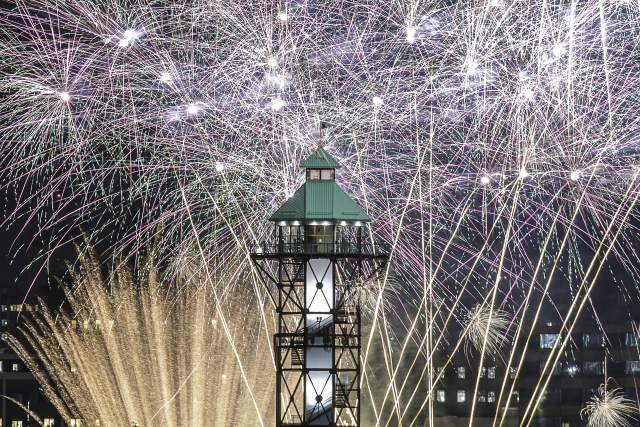 Colorful fireworks bursting around a large tower on a waterfront