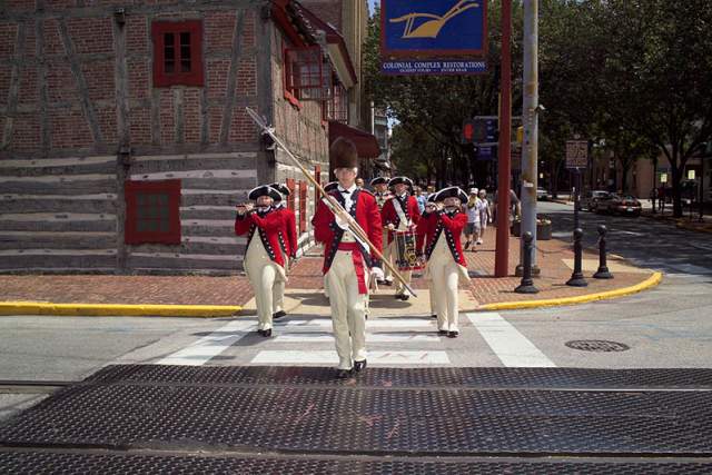 A group of men dressed as colonial soldiers in a crosswalk on a street