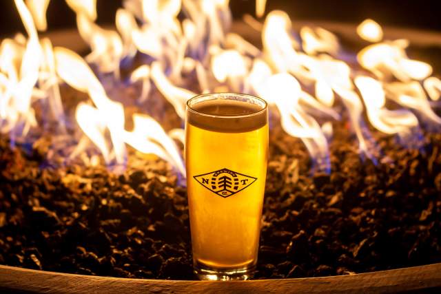 Glass of beer sitting on the side of a burning firepit