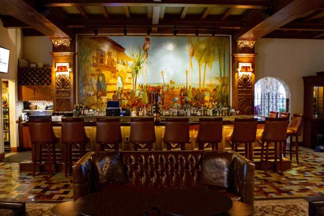 A leather couch in front rustic bar with a large painting overhead at The Hotel Hershey.
