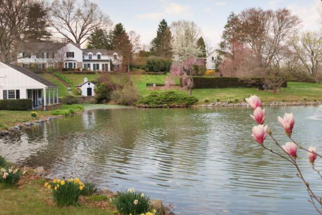 Exterior of a large white mansion on a hill with a pond in front