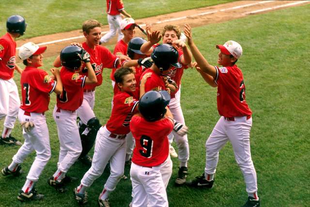 A group of young boys in baseball uniforms cheering and hugging one another