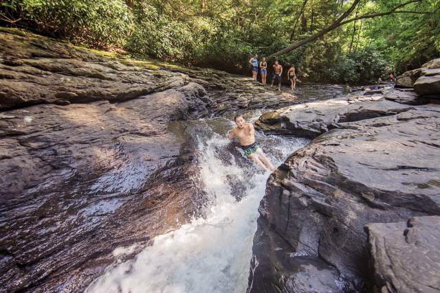 Young kids sliding down a natural waterslide in a river with large boulders on either side